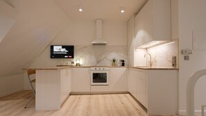 A modern kitchen with white cabinetry, a built-in oven, and a television mounted on the wall. - Boutique Charme Apartments 10 (Baden-Baden)