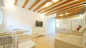 A modern living room with wooden beams, a television on a cabinet, a dining area with chairs and a table, and a sofa. - DolceVita Apartments N. 413 (Venice)