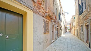 A narrow cobblestone street flanked by historic buildings with a green door and a metal gate. - DolceVita Apartments N. 413 (Venice)