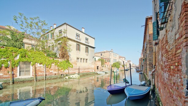 A canal with boats docked, buildings along the water, and a clear sky. - DolceVita Apartments N. 413 (Venice)