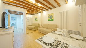 A modern living room with a wooden ceiling, a sofa, a dining table set for two, and a kitchen area with a microwave. - DolceVita Apartments N. 413 (Venice)