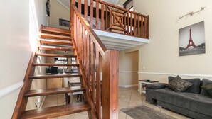Eine Holztreppe führt zu einer oberen Etage, ein graues Sofa und ein gerahmtes Bild vom Eiffelturm an der Wand.