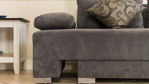 Ein graues Sofa mit einem gemusterten Kissen und einem passenden Hocker, platziert neben einem weißen Beistelltisch mit einem blauen Gegenstand darauf.