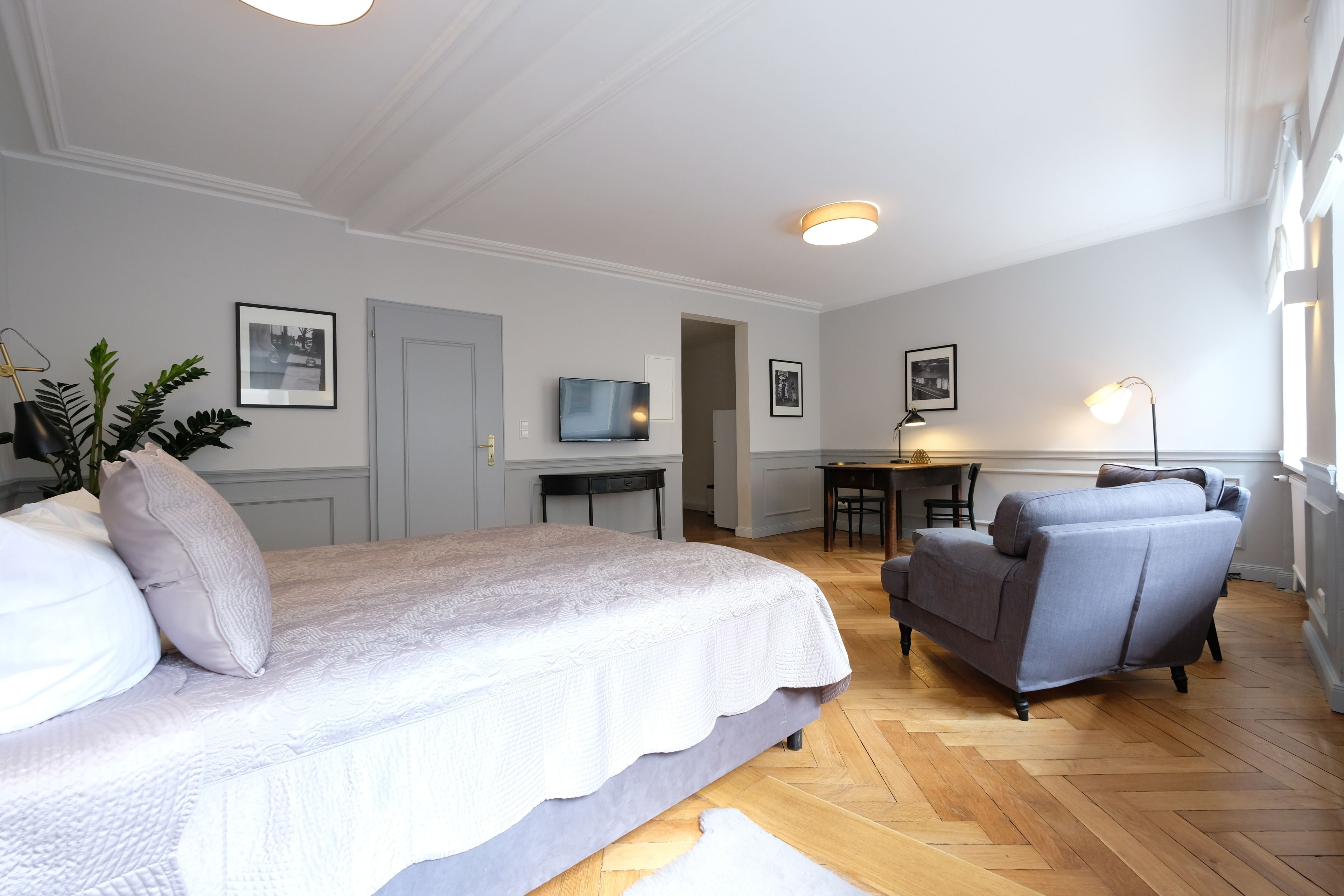 Ein Schlafzimmer mit einem Bett, einem grauen Sessel, einem Schreibtisch und einem Fernseher.