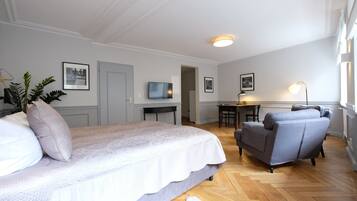 Ein Schlafzimmer mit einem Bett, einem grauen Sessel, einem Schreibtisch und einem Fernseher.