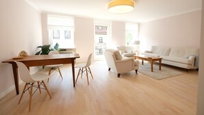 A spacious living room with a wooden dining table, white chairs, a white sofa, and a coffee table. - Boutique Charme Apartments 14 (Baden-Baden)