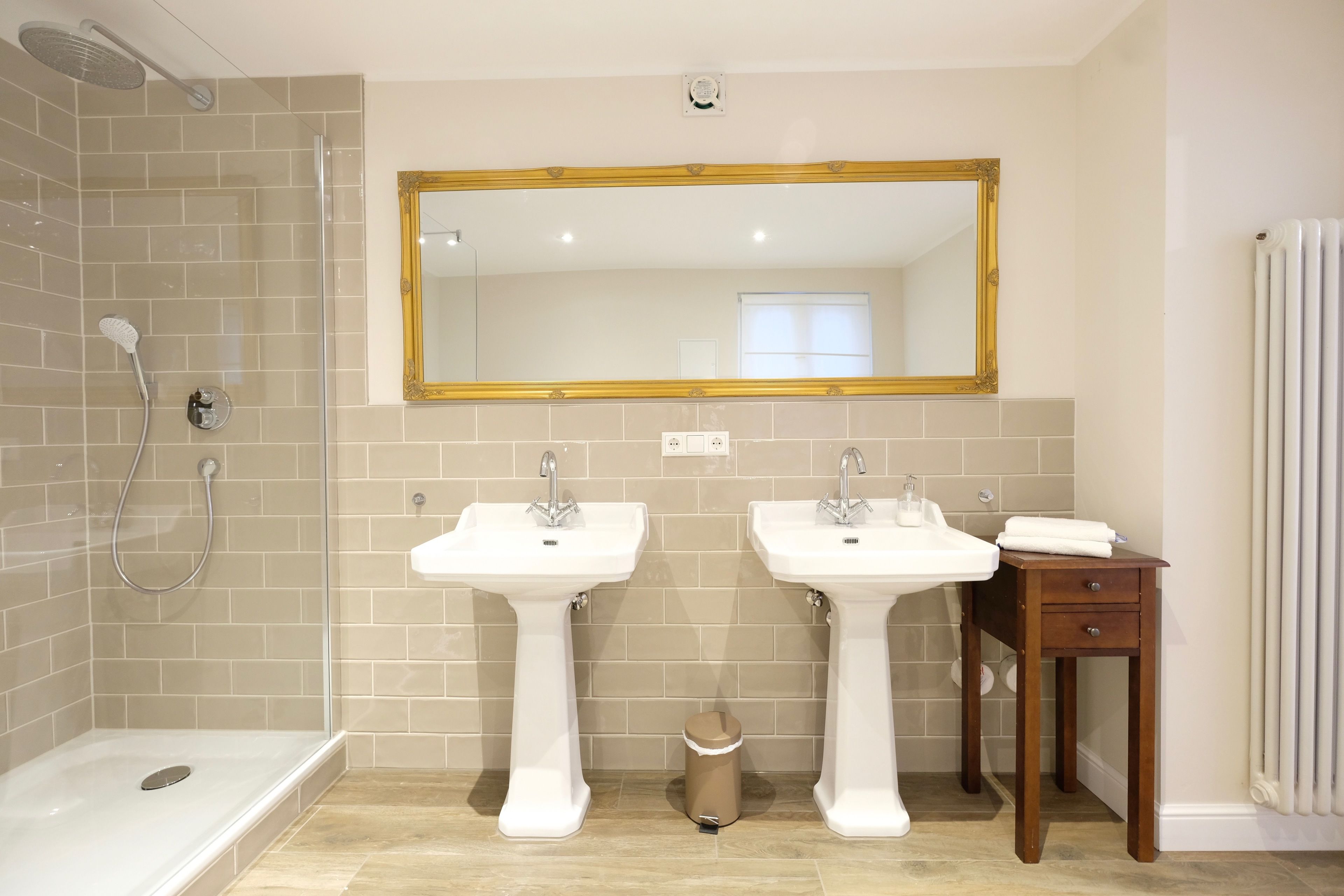 Une salle de bain avec deux lavabos, une douche, un miroir et un radiateur.