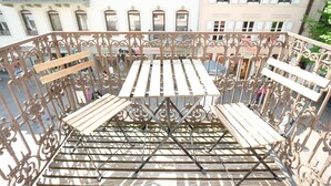 A balcony with a wrought iron railing, a wooden table, and two wooden chairs. - Boutique Charme Apartments 14 (Baden-Baden)