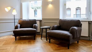 A room with two armchairs, a small table, and a floor lamp. There are windows with views of buildings outside. - Boutique Charme Apartments 14 (Baden-Baden)