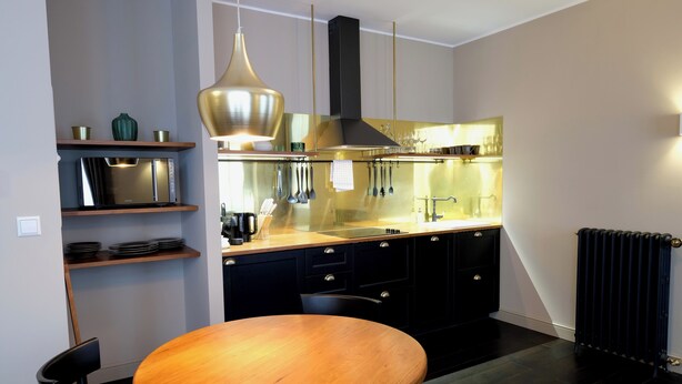 A modern kitchen with a round wooden table, black cabinets, stainless steel appliances, and pendant lighting. - Boutique Charme Apartments 5 (Baden-Baden)
