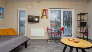 Una habitación moderna con una cama, una mesa de comedor con sillas, un televisor en la pared y una estantería.