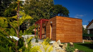 Una cabaña de madera con techo rojo, rodeada de follaje y rocas.