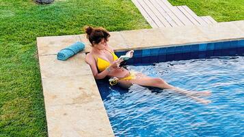A person relaxing by a pool with a grassy area and plants around.