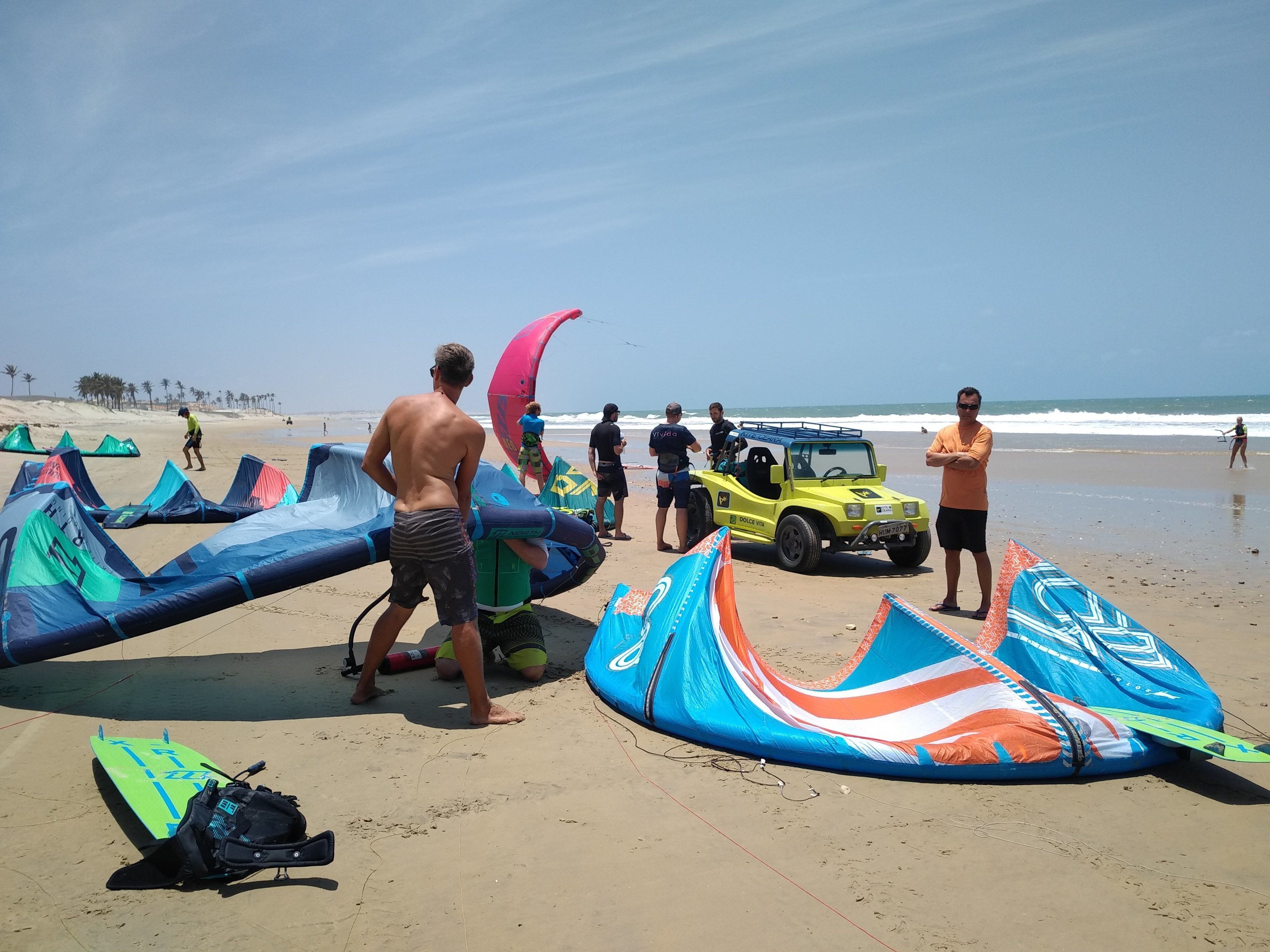 A beach with several colorful kites and a yellow vehicle.