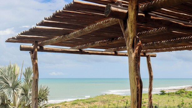 Una pérgola de madera sobre una piscina con vistas a la playa y al océano.