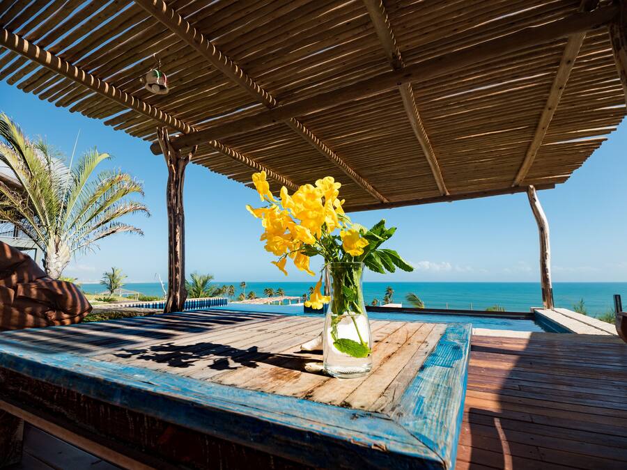 A wooden deck with a clear view of the ocean and a wooden pergola overhead.