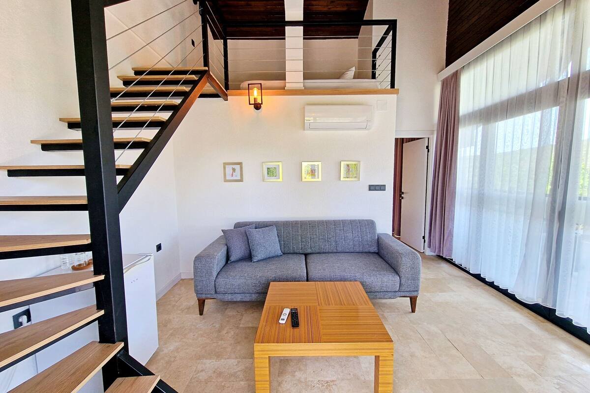 A modern living room with a grey sofa, wooden coffee table, and a staircase with black railings.