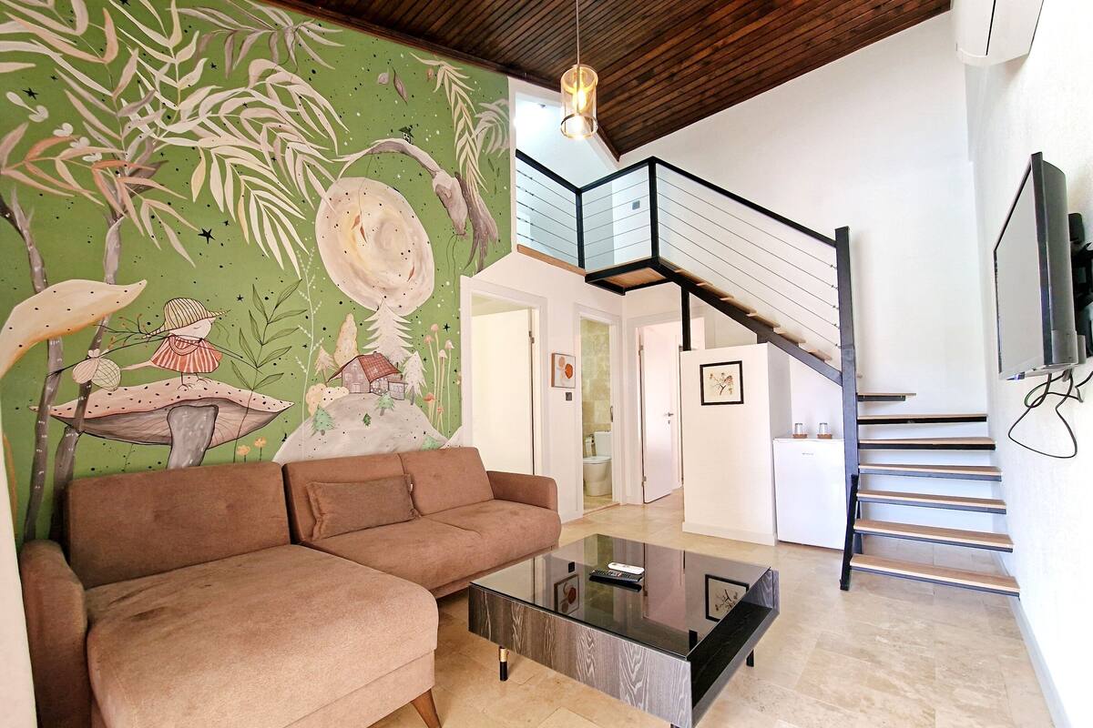 A living room with a brown sofa, a glass coffee table, and a mural on the wall.