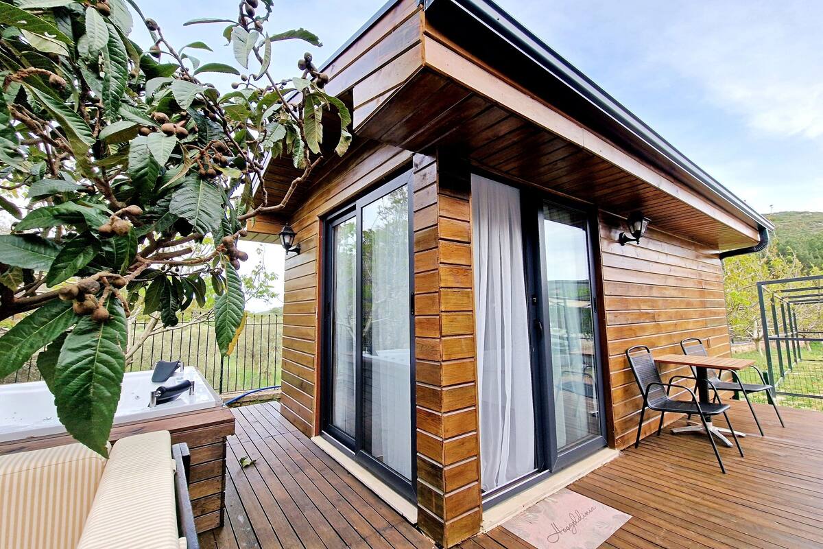 A wooden cabin with a deck, large windows, and a patio area with a table and chairs.