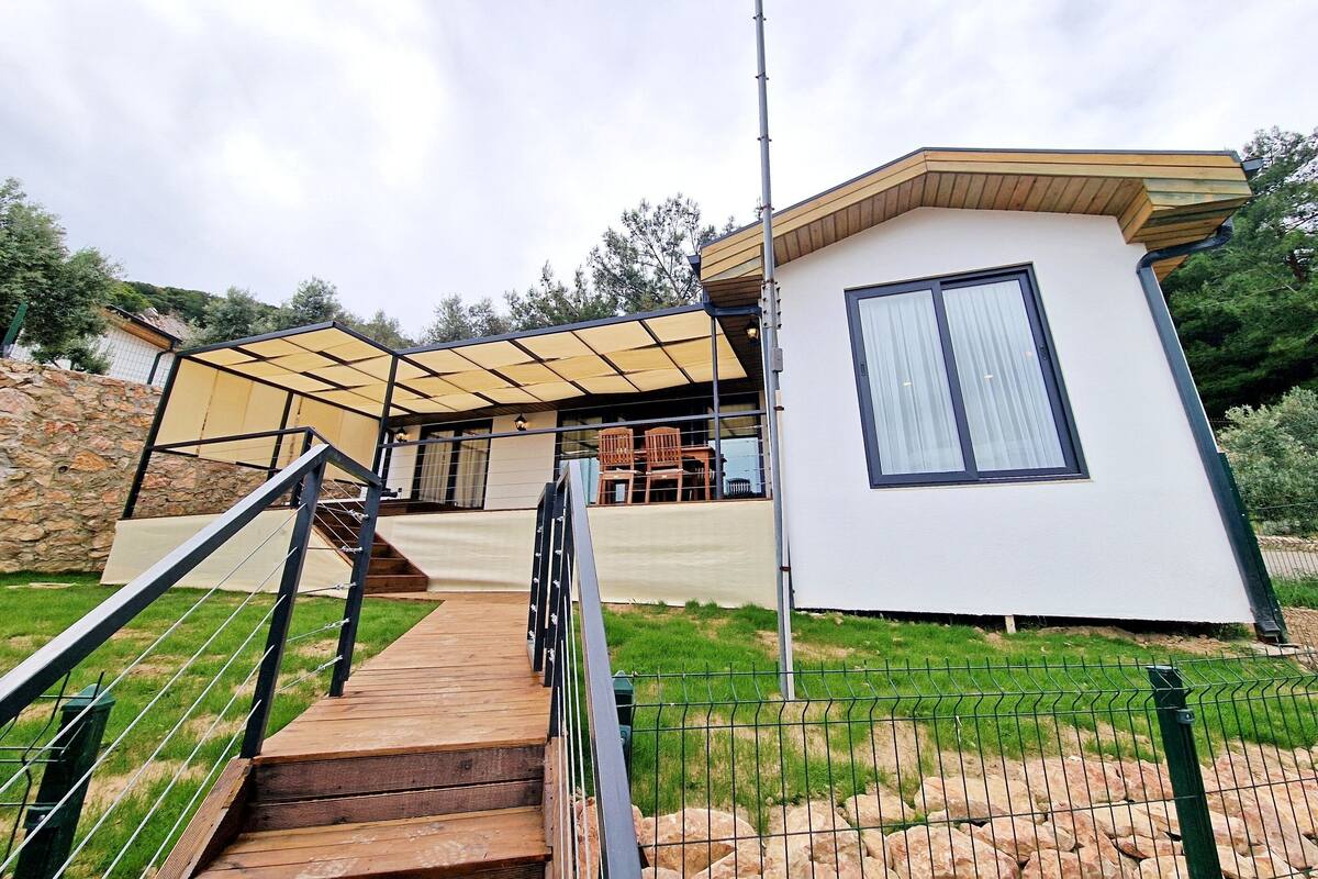 A modern house with a covered patio, a staircase, and a fenced garden area.