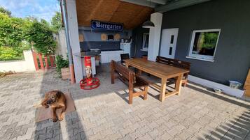 En utesittplats med ett träbord och bänkar, en hund som ligger på marken och en skylt med texten ”Biergarten”.
