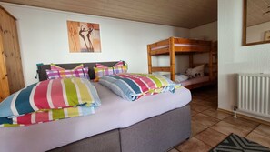 A room with a bunk bed, a single bed with colorful striped bedding, a painting on the wall, and a radiator.