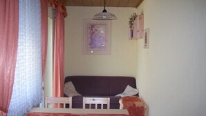 A room with a bed, a table with chairs, a hanging light fixture, and a framed picture on the wall.