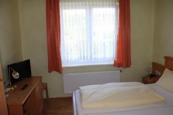 A bedroom with a bed, a nightstand, a desk with a lamp, and a window with curtains. - Zur Rotenfelsstube (Traisen)