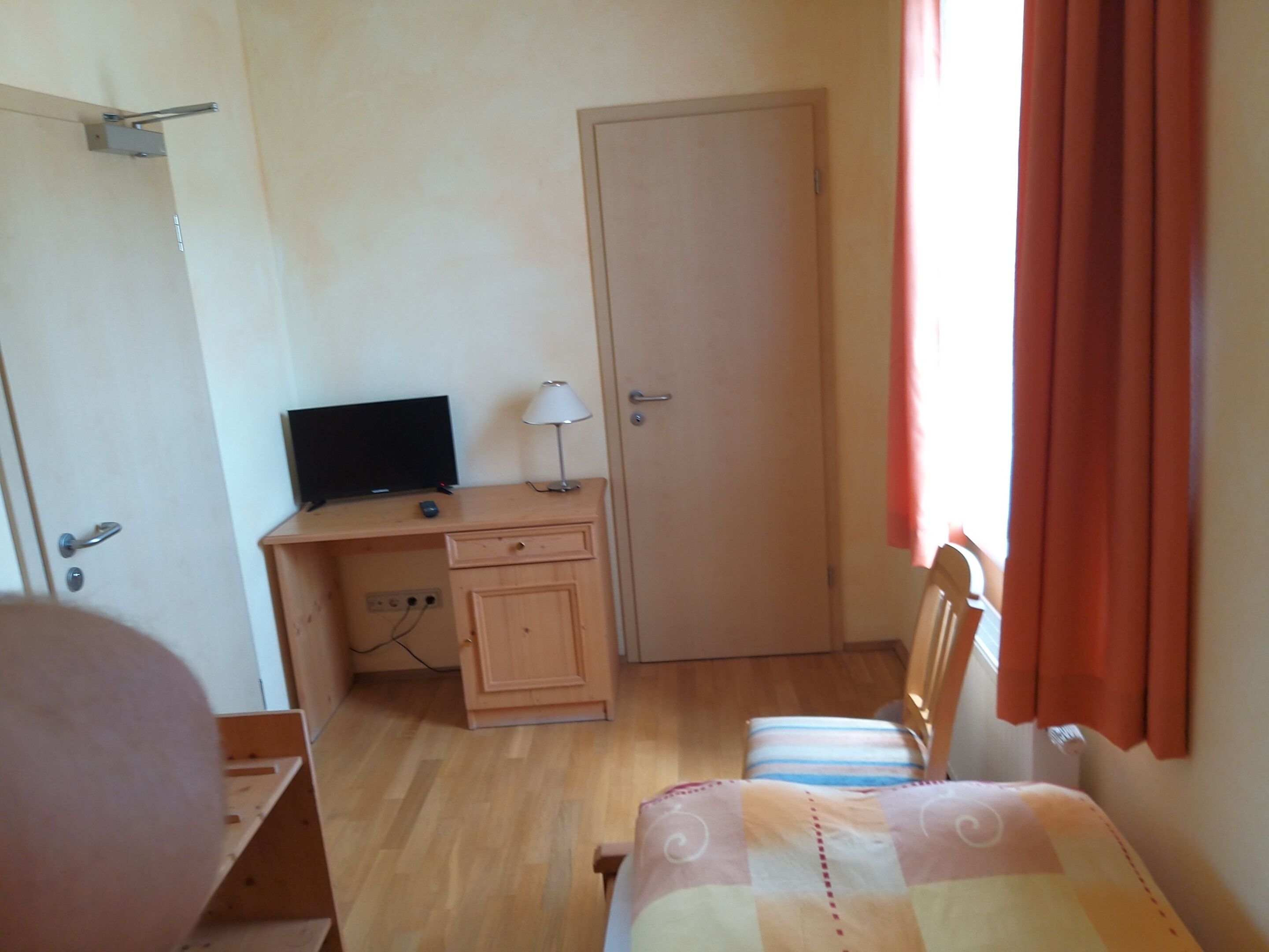 A bedroom with a wooden desk, a television, a lamp, a door, and a bed with striped bedding.