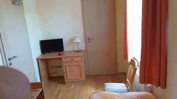 A bedroom with a wooden desk, a television, a lamp, a door, and a bed with striped bedding.