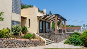 A modern house with a stone staircase leading to a covered patio with outdoor furniture. - Villa Kommeno (Corfu)