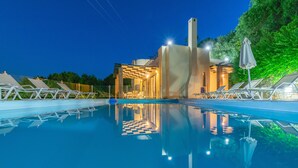 A swimming pool with lounge chairs and a building with a checkered floor in the background. - Villa Kommeno (Corfu)