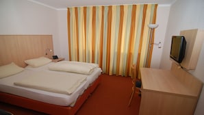 A hotel room with two beds, a desk, a TV, and a lamp. - Catharinenberg (Molfsee)