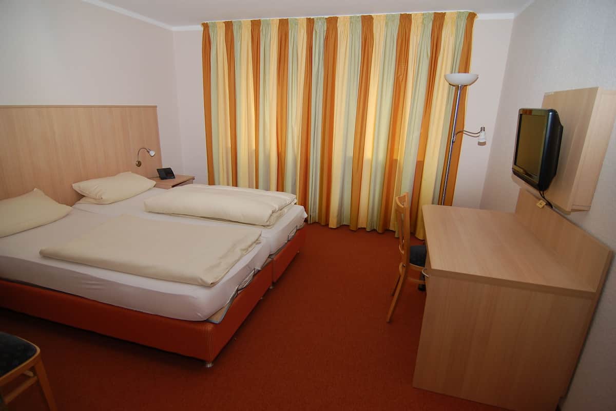 A hotel room with two beds, a desk, a TV, and a lamp.