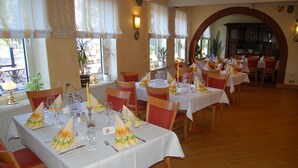 A restaurant with multiple tables set for dining, featuring white tablecloths and red chairs. - Catharinenberg (Molfsee)