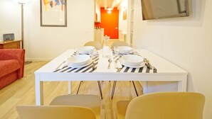 A dining area with a white table set for four, including plates, glasses, and cutlery. There is a red sofa and a lamp in the room. - DolceVita Apartments N. 443 (Venice)