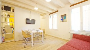A room with a dining table, chairs, a TV mounted on the wall, and a red sofa. - DolceVita Apartments N. 443 (Venice)