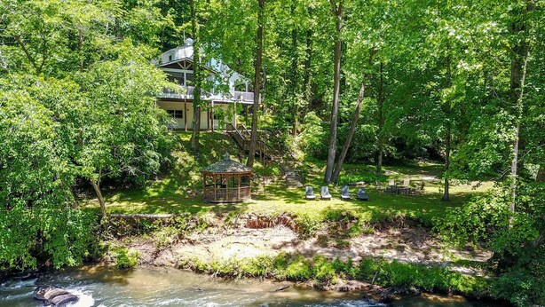 A house with a deck overlooking a river, surrounded by dense greenery. - Stunning Rushing River Views  ~ North Georgia Mountains ~ Short Hop to Town! (Dahlonega)
