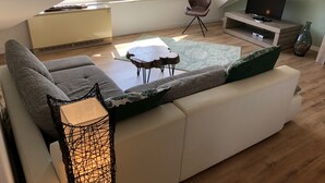 Eine moderne Loft-Wohnung mit großem Fenster, einer Sofagarnitur, einem Fernseher und einem kleinen Tisch.