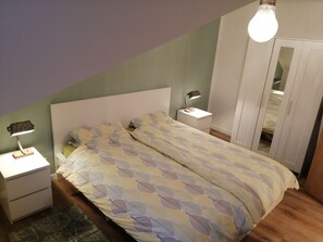 A bedroom with a bed, two bedside tables, a nightstand, a lamp, a wardrobe, and a hanging light fixture. - Apartment Katya (Winterberg)