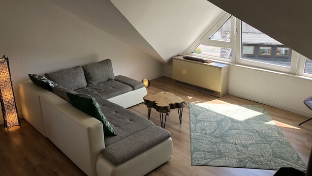 Ein modernes Schlafzimmer im Loftsstil mit schrägverdeckter Decke, einer Eckcouch, einem kleinen runden Couchtisch und einem großen Fenster, das für natürliches Licht sorgt.