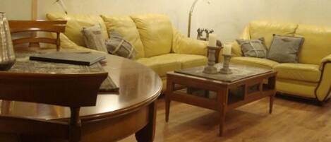 Una sala de estar con un sofá amarillo, una mesa de centro de madera y una mesa de comedor con sillas.