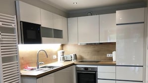 Eine kleine Küche mit weißen Schränken, einem Einbauofen, einer Mikrowelle und einem Kühlschrank.