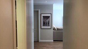 Ein Flur mit Holzboden, der in einen Wohnbereich mit einer Couch und einem gerahmten Bild an der Wand führt.