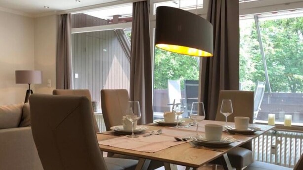 Ein Essbereich mit einem Tisch für vier Personen, umgeben von Stühlen, einer Lampe und Blick ins Freie.