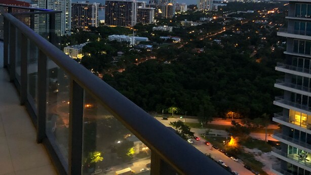 A cityscape at dusk with high-rise buildings, a view of the water, and a balcony railing. - Amazing Luxury Apartment at the 5 Star Hotel (Miami)