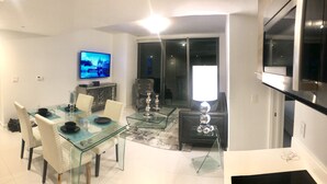 A modern dining area with a glass table and chairs, a flat-screen TV on the wall, and a kitchen area with a Bosch refrigerator. - Amazing Luxury Apartment at the 5 Star Hotel (Miami)