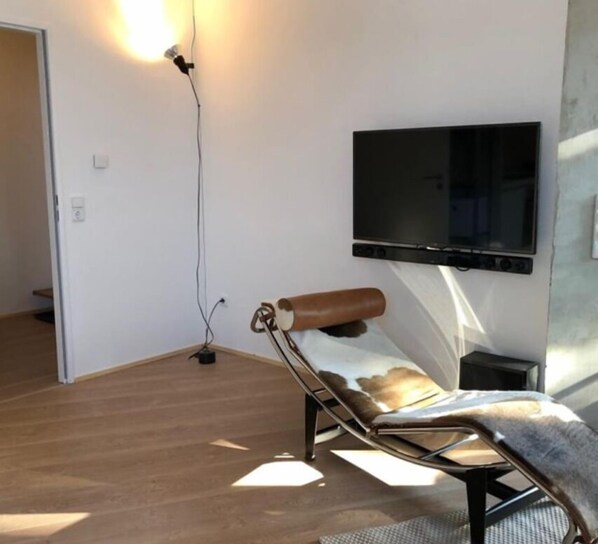 Ein modernes Zimmer mit Holzboden, einem an der Wand befestigten Fernseher und einem Massagesessel.