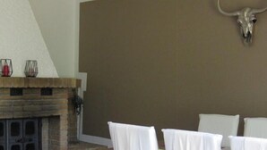 Un comedor con chimenea de piedra, sillas blancas y decoración de cráneo de toro en la pared.