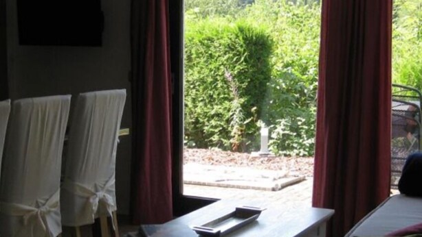 Habitación con cama, una mesa con un control remoto y vistas a un jardín a través de amplias ventanas.